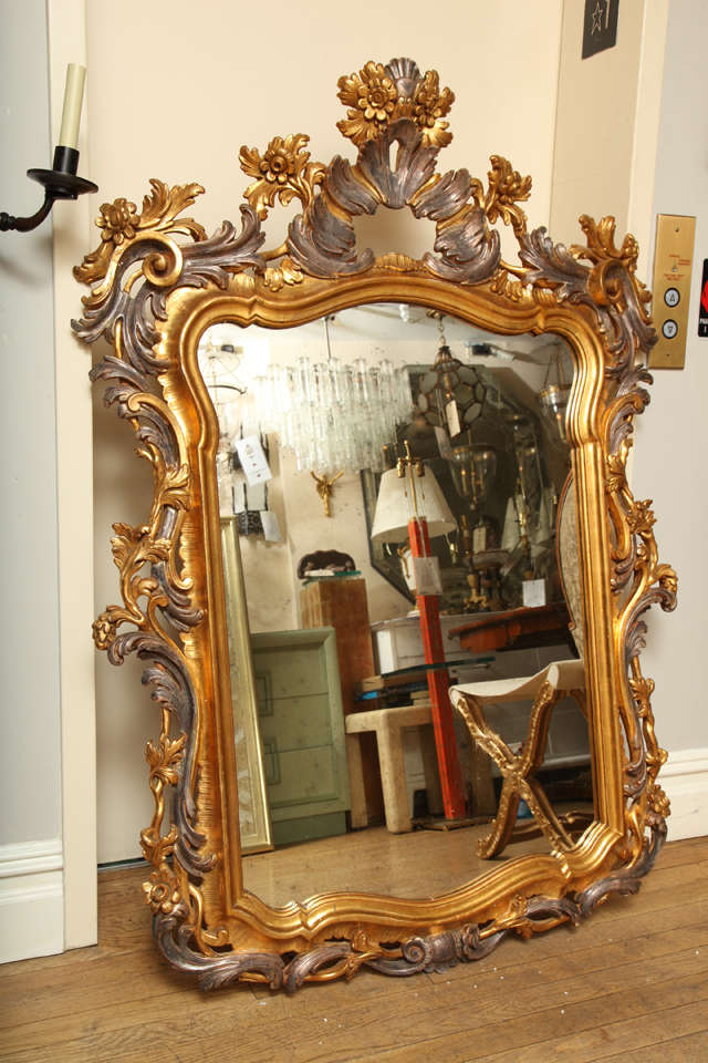 An Italian carved and giltwood Rococo style mirror with silver gilt details, the frame with scroll, leaf, and floral motifs. 