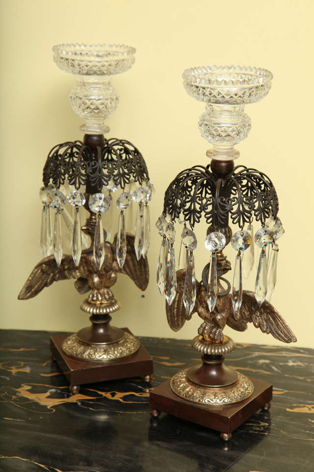 Very fine pair of Regency ormolu, bronze and cut crystal candlesticks, the diamond cut crystal urn-form nozzle above a star and prism-hung pierced bronze anthemia-banded canopy, supported by a gilt bronze spread-winged eagle with a coiled serpent in