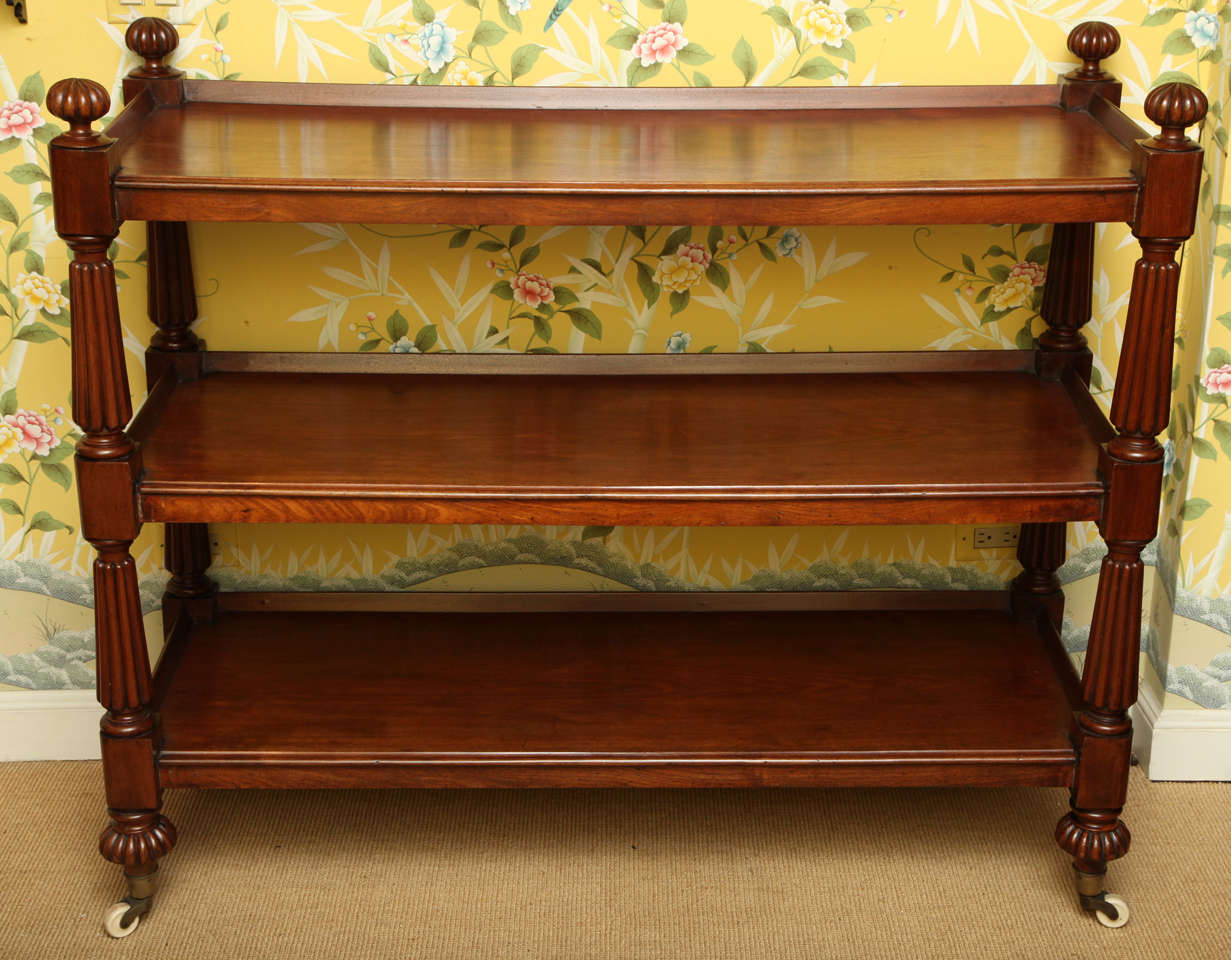 Fine William IV carved mahogany three tier whatnot, the three-quarter galleried shelves with thumb mouled front edges, having shaped block end pieces on eight tapering reeded columnar supports with round reeded finials and feet, on brass cup