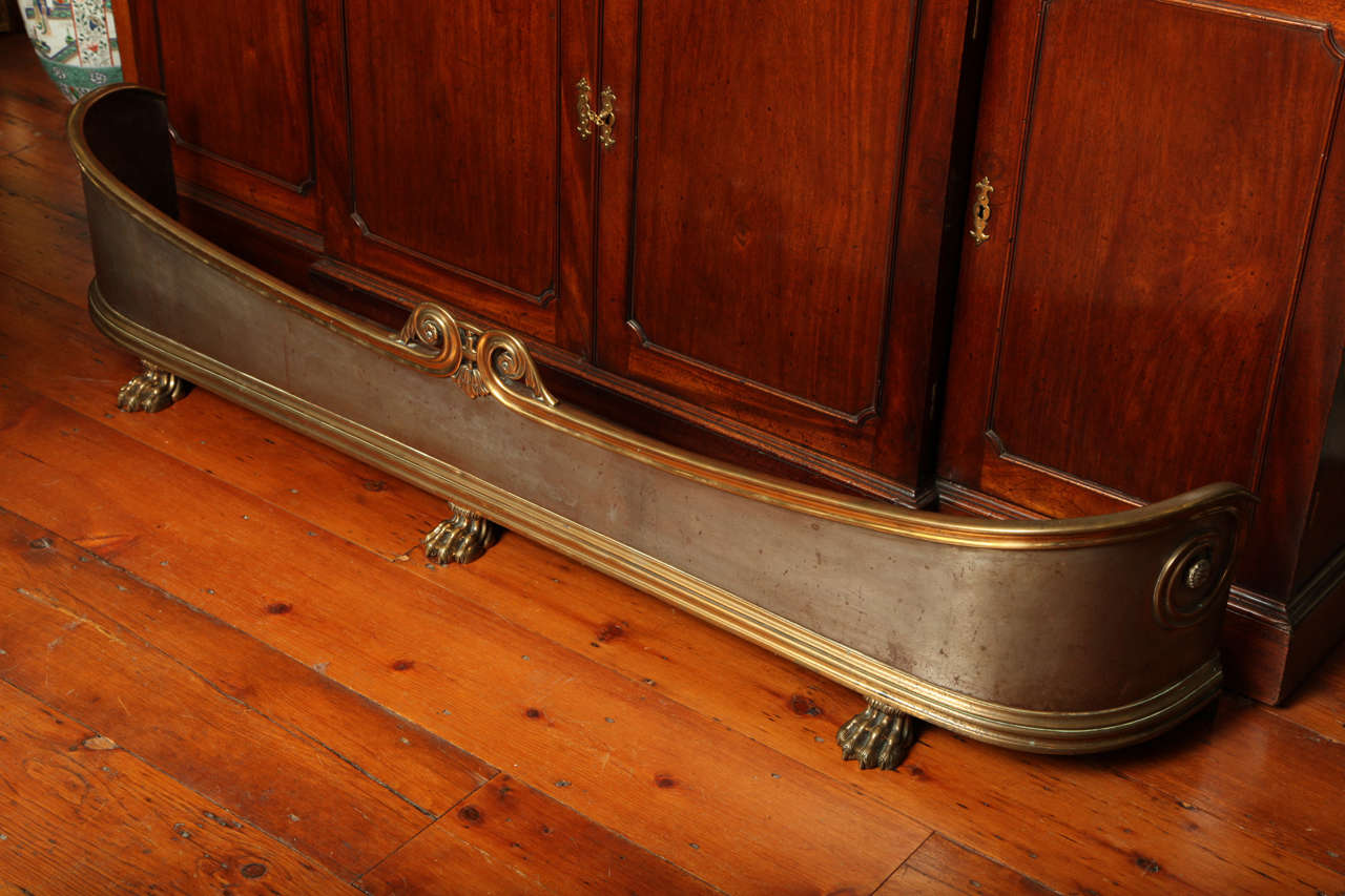 Very fine large Regency period incurvate brass and steel fire fender, the top with a central pendant leaf motif flanked by outscrolling leaves with flower head centers, with brass mouldings top and bottom, raised on three brass lion's paw feet.