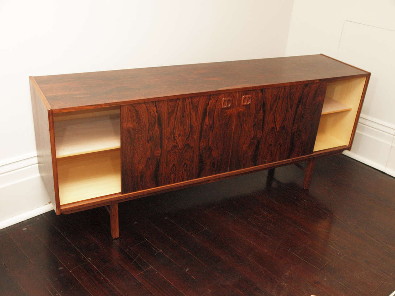 Low rectangular credenza in rosewood veneer; four central drawers flanked by two cabinets, each with one shelf; sliding doors at either side; 