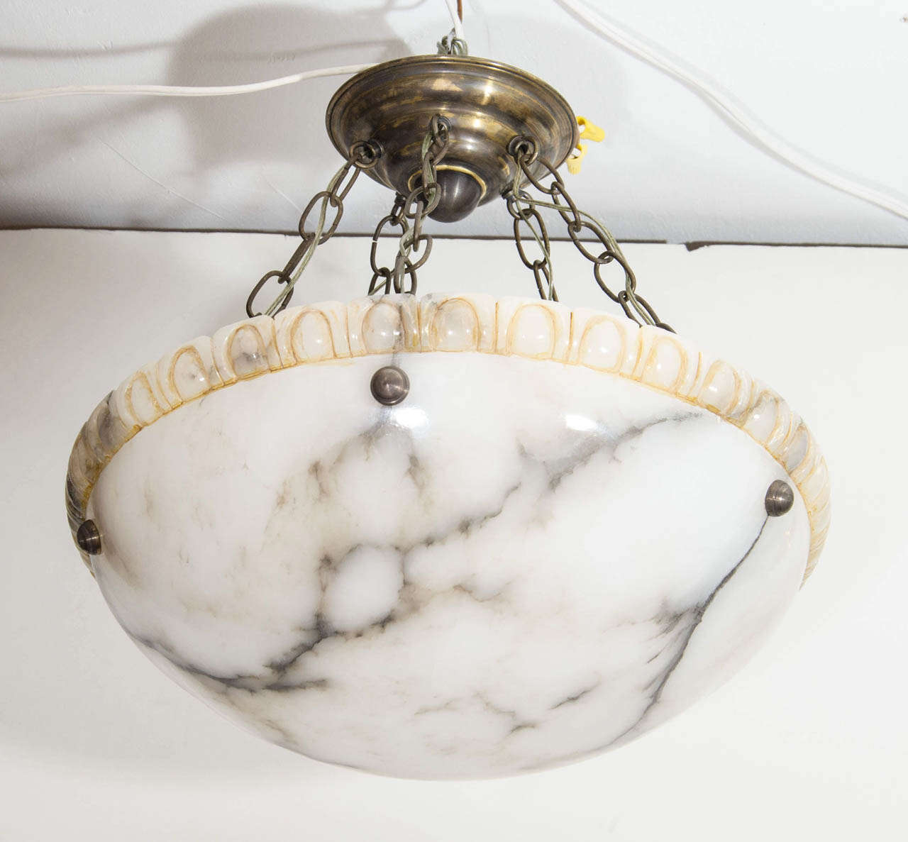 Creamy white alabaster, lined with charcoal mineral veining, this fixture is crowned with a decorative, dental-style upper rim, enriched with umber tones. Suspended on five original chains, brass canopy and hardware, the fixture may be custom wired