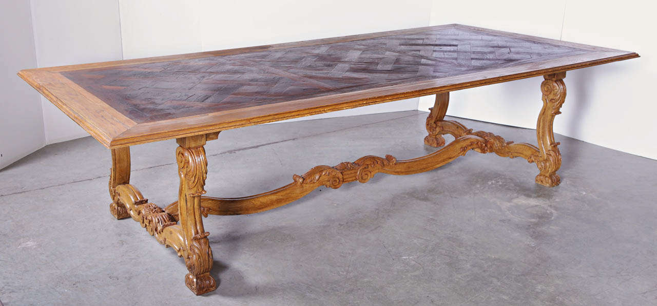 This large antique French table is in the Regence Style and accommodates ten to twelve people depending upon the size of the chairs.  The top has an old parquet section of flooring inset into it, with a series of different sized finished planks