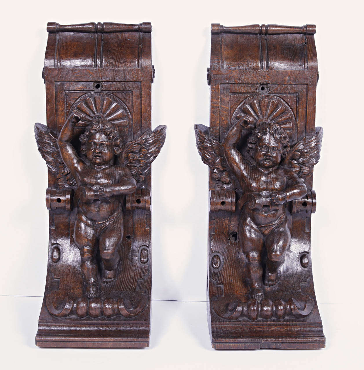 This stunning pair of French hand carved, decorated, oak corbels depict cherubs within an elongated, incurved stylized cartouche.  Above their heads is a stylized palmette, and their are arms rest upon the upper portion of a c-scroll. The wings wrap