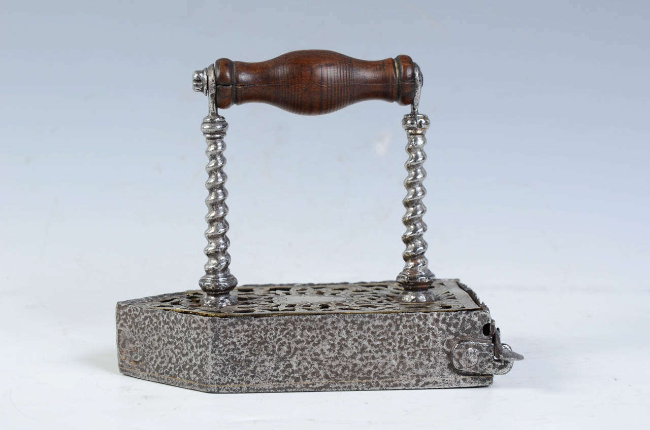 Flatiron in which where placed a bar of heated metal.
The body of iron is decorated with an openwork and engraved brass plate (crest, volutes, pots of fire).
the turned wood handle is maintained by two twisted columns.