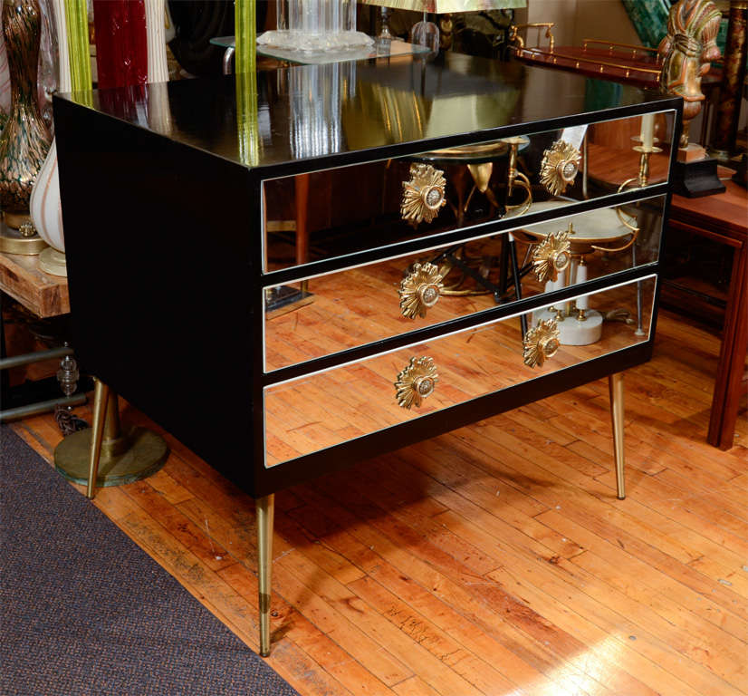 A vintage dresser in black lacquered wood with three mirror-fronted drawers and brass legs. Each drawer has two brass 