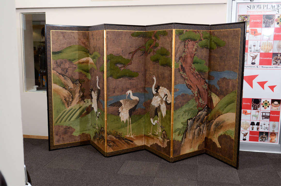 A Japanese six panel folding screen, or byobu. The piece is decorated with a grouping of cranes in a traditional Japanese landscape