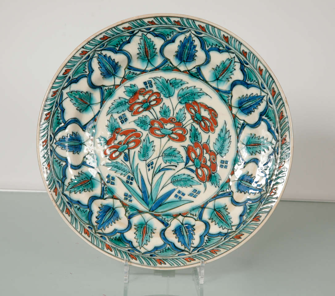 Pottery charger with Iznik inspired polychrome floral decoration in green, blue and red. The edge has a striped design.
