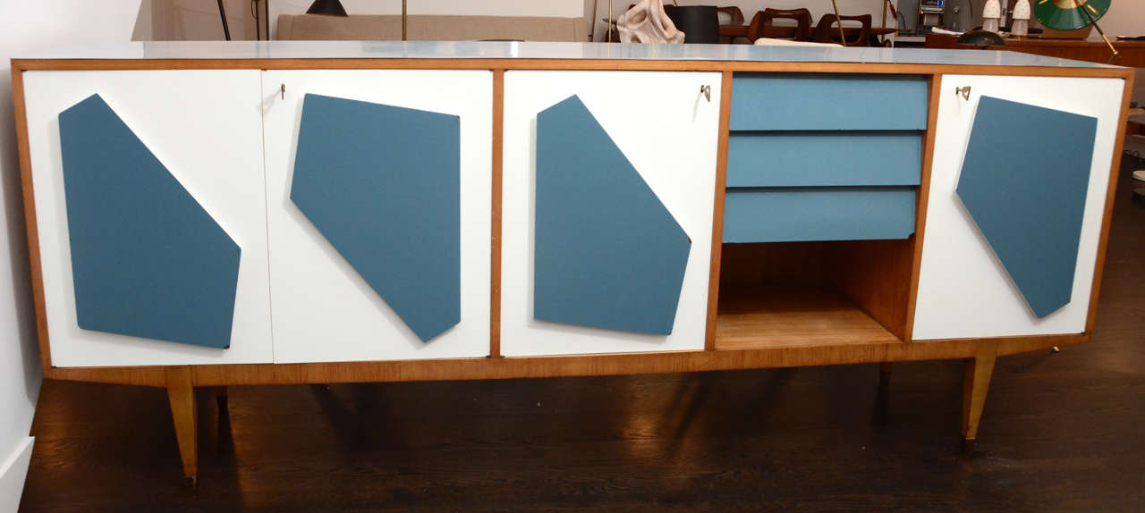 This unique credenza is beauty and function at its best. Artistic shapes are laminated blue on the four white doors behind which are shelves and drawers. Early example of Italian laminates on birch with veneers. All original including the door