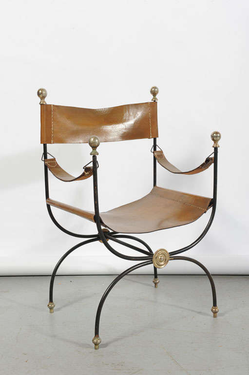 A wrought iron and saddle stitched leather chair and ottoman with brass details.