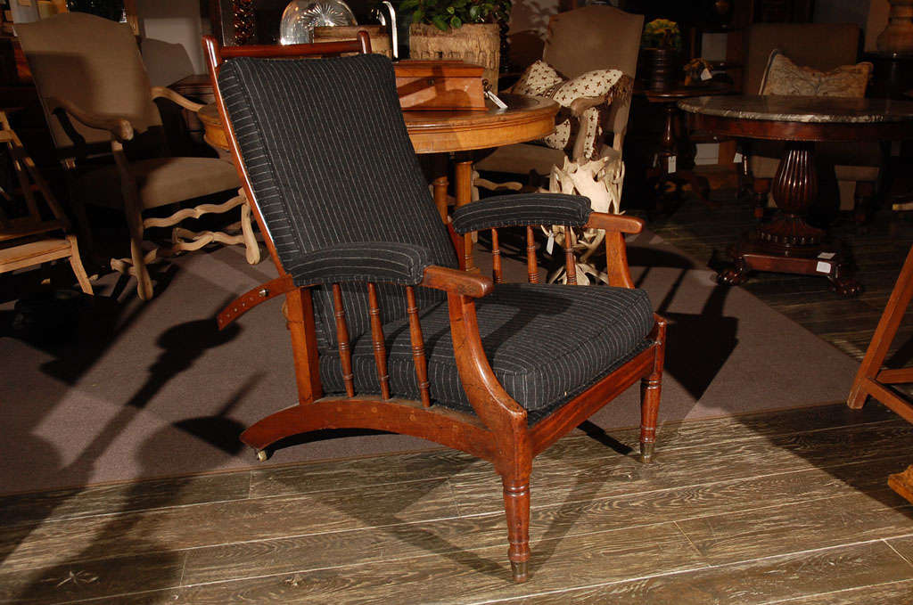 A handsome mahogany spindle side recliner with a brass rod for seven points of recline, brass back castors, and front ring-turned legs. Upholstered in custom slate and bone pinstripe