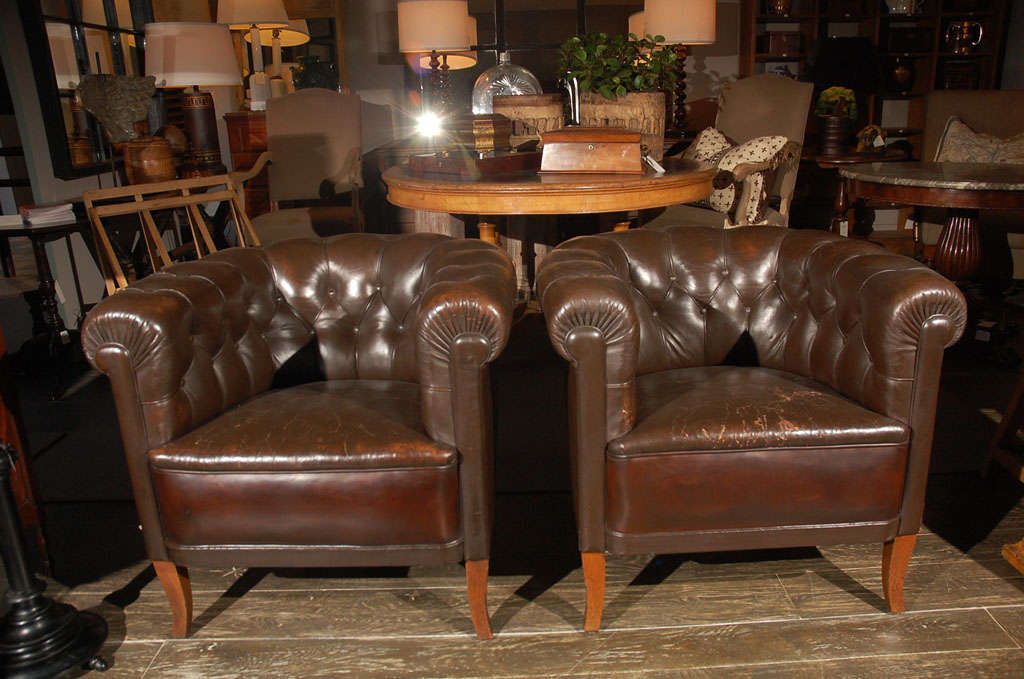 A pair of tufted leather club chairs of a lighter proportion with a horseshoe back and flared legs