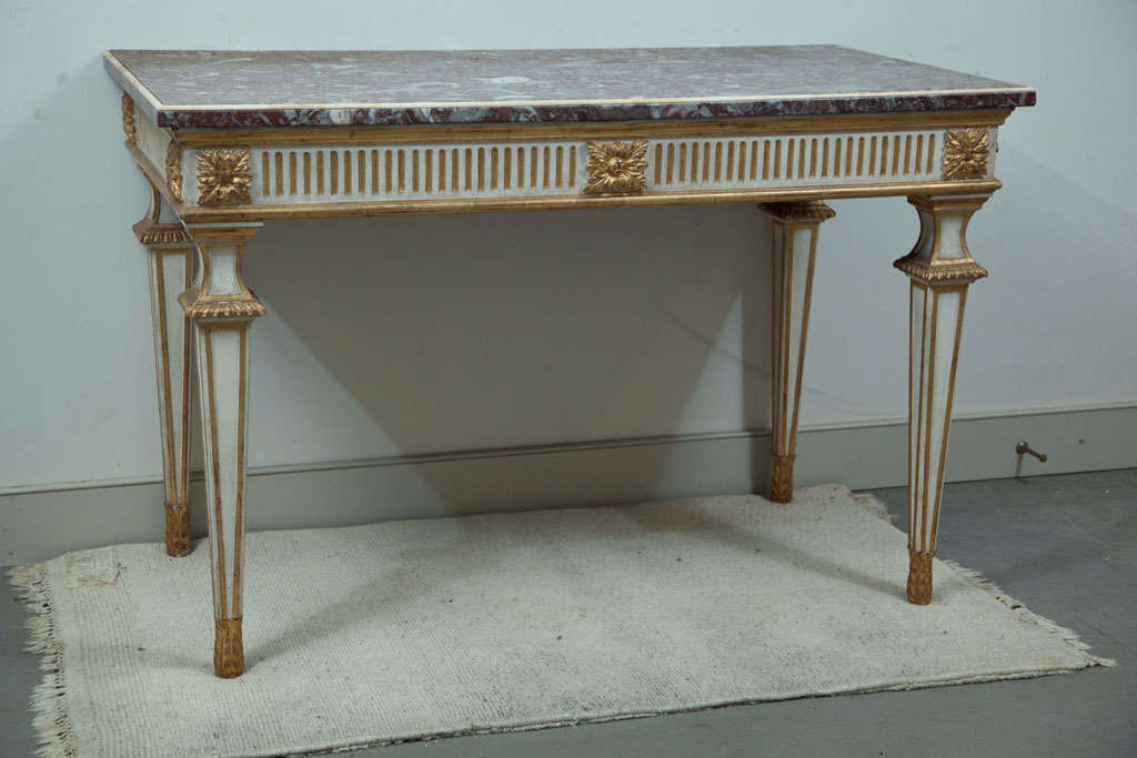 Cette belle table néoclassique peinte en crème et dorée à la feuille présente un tablier cannelé avec des sculptures de feuillage, tandis que le plateau en marbre rose est bordé de perles de marbre crème. Parfaitement dimensionné pour un grand hall