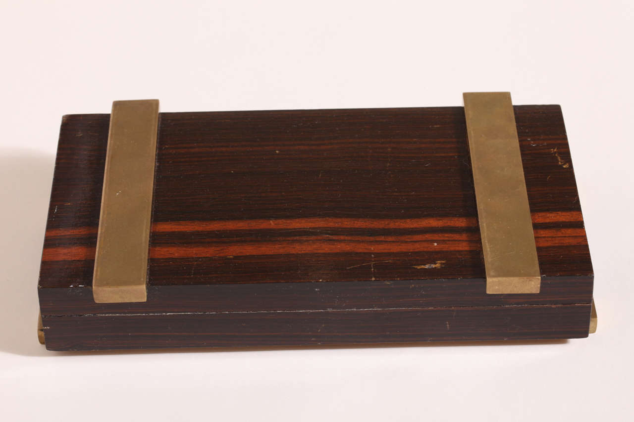 Macassar ebony veneered cigarette box with two horizontal brass bars underneath and two vertical brass bars on top.

Impressed underneath DESNY PARIS/ MADE IN FRANCE/ DEPOSE.
Provenance: Collection du Chateau de Gourdon.