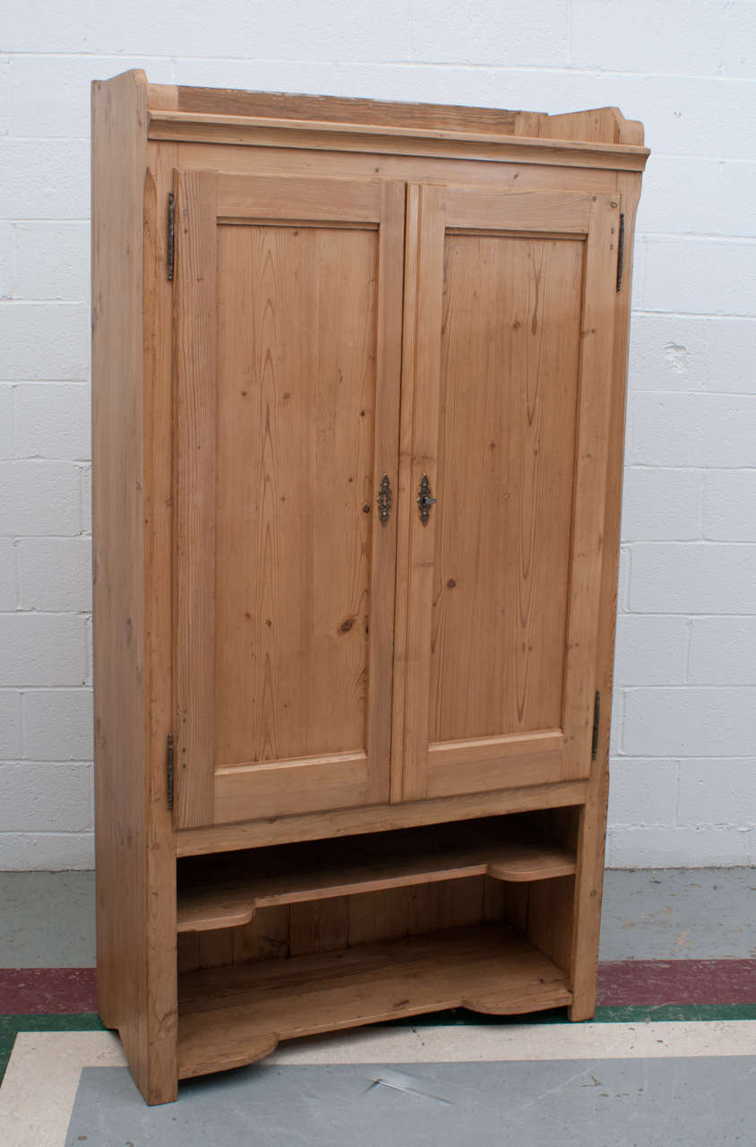 An unusual pine cupboard featuring a gallery top for display or storage and two panelled doors opening to a morticed fitted interior. The lower open section is intended for shoes but is useful for office machines etc.