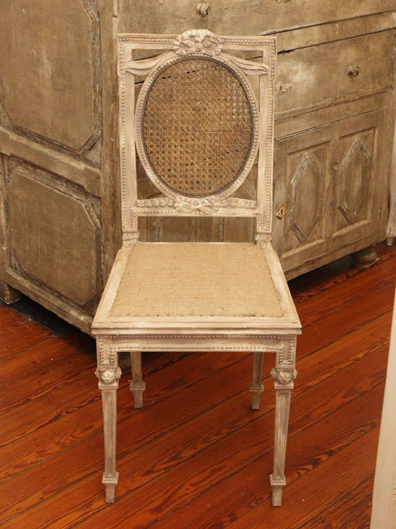 Charming Louis XVI chair with caned back and carved details throughout.  Painted in a pale grey white with soft patina.  Burlap upholstered seat.