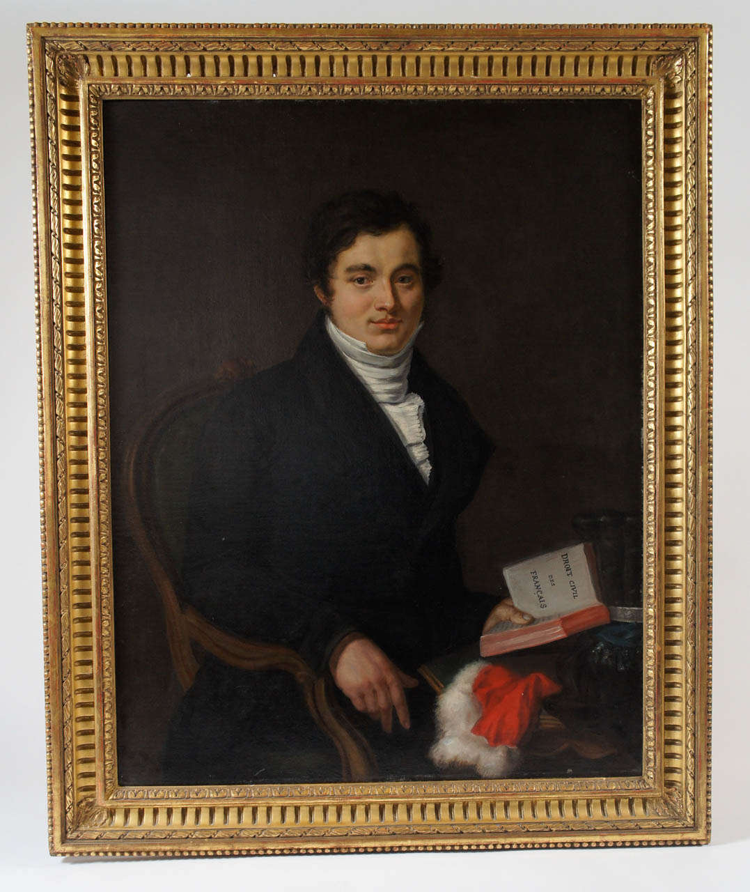 Early 19th century French oil on canvas portrait of a handsome young 'juriste' of the Napoleonic Code shown seated in upholstered Louis XV style chair at table with feathered cap and fur-trimmed gown in three-quarter profile pose holding an open