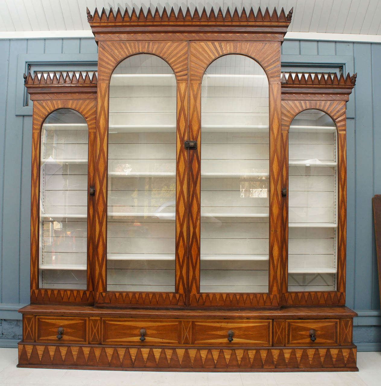 Uncommon circa 1870 large breakfront form cabinet of slim profile having full parquetry geometric veneers in mahogany, chestnut, oak, and walnut. Top cornices having triangular crenellation with canted spike finial corners above projecting central