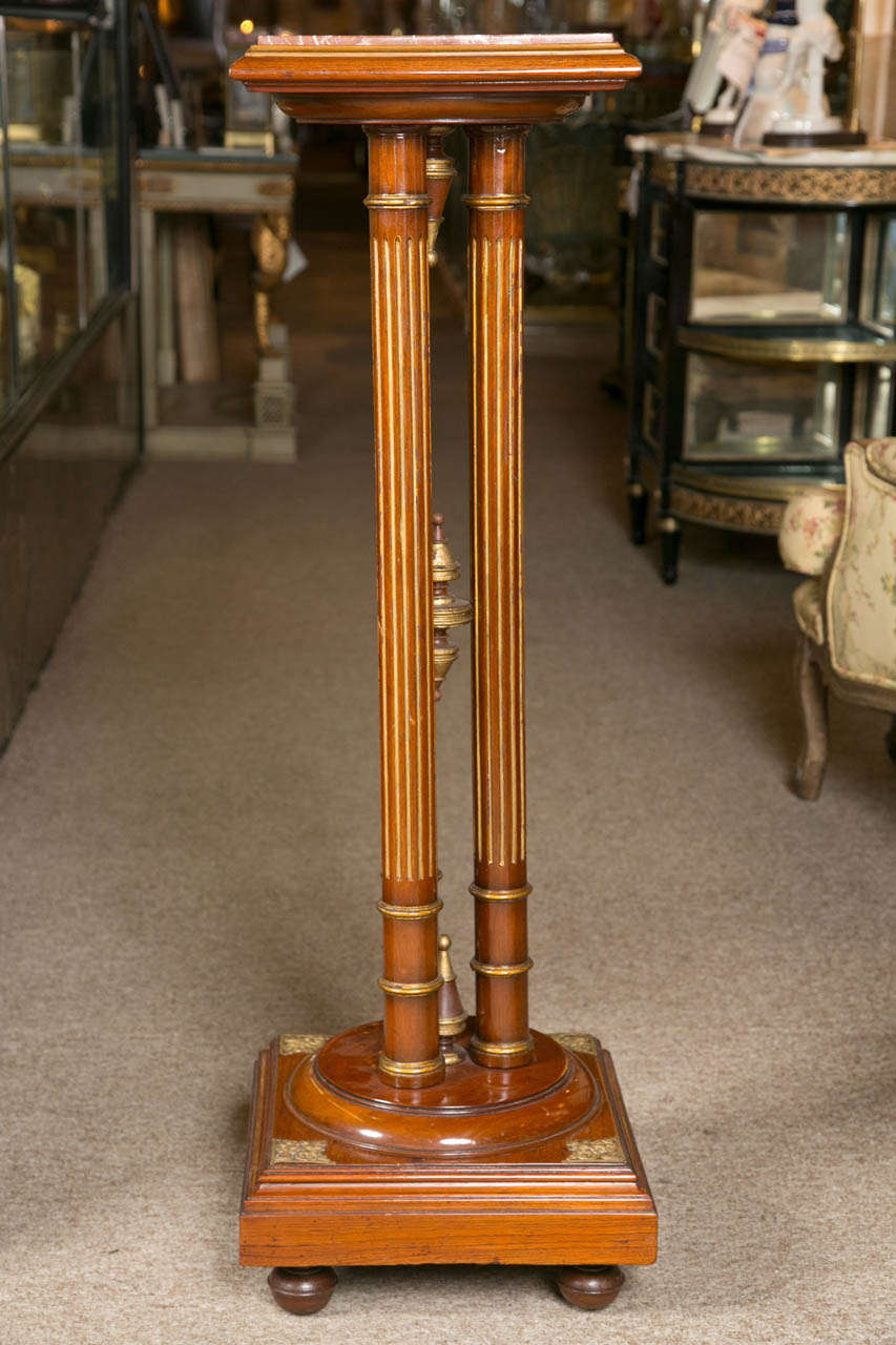 Pair of Regency style mahogany column pedestals, the square marble set in a molded top, supported on three fluted circular uprights joint by a finial stretcher, raised on a block plinth decorated with brass accents.