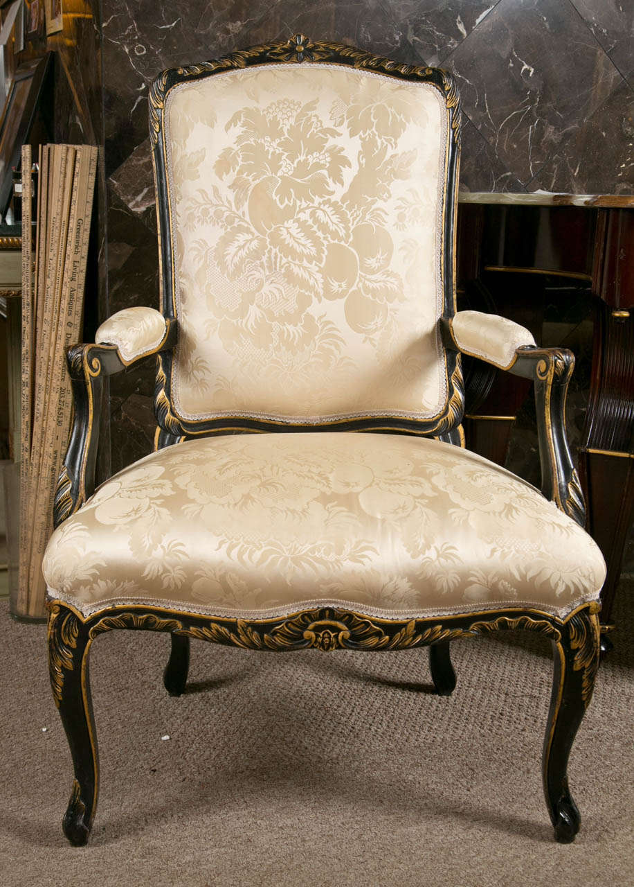 Pair of French fauteuils in the Louis XV style, the frame ebonized with parcel-gilt, padded back with down-swept arms, upholstered in champagne color silk, raised on cabriole legs.