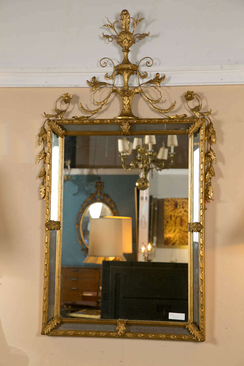 French classical style gilded mirror, second quarter of 20th century, the rectangular plate surmounted by a mirrored shield-panel and annulated band, the top decorated with carved trophy crest and laurel branch motif.