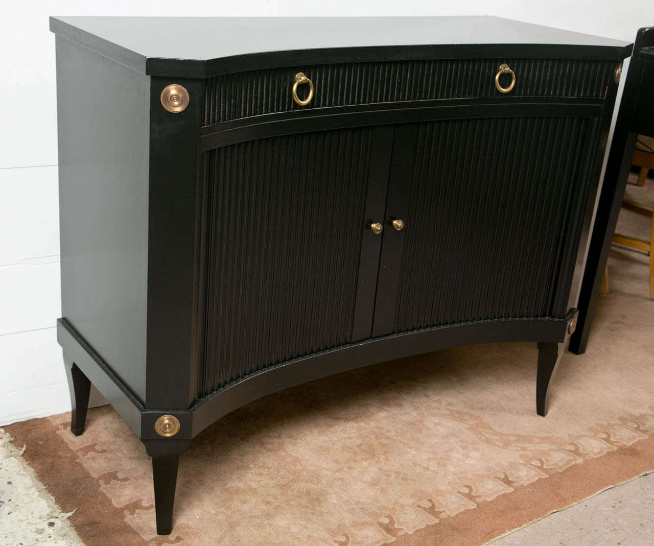 An overall ebonized cabinet in the Hollywood Regency taste, circa 1960s, the convex top over a narrow frieze fitted with a single drawers, over a conforming cabinet fitted with two doors opening to a single shelving interior, raised on pegged feet.