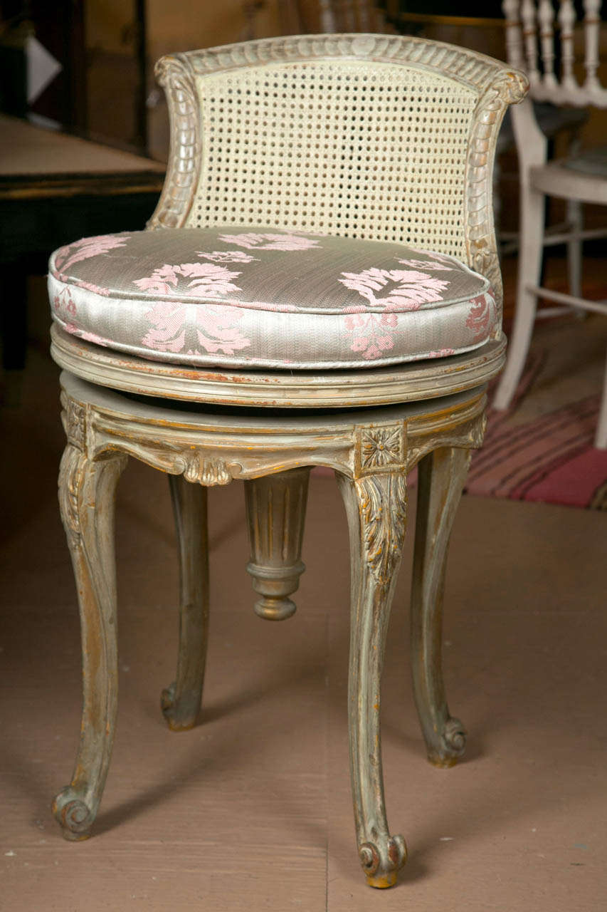 A pretty petite Louis XV style piano swivel stool. The fine white washed frame finely carved. The back and seat caned. The seat accompanied by a silk cushion. By Maison Jansen