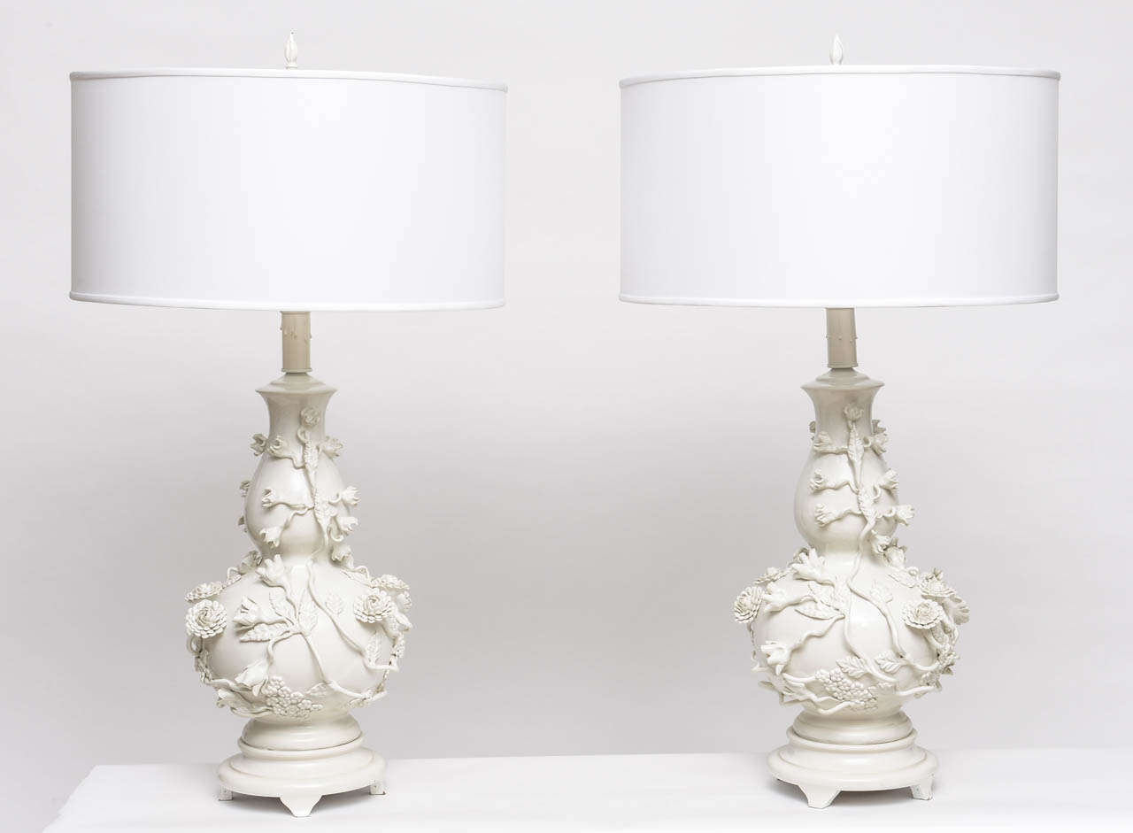 Pair of large Blanc de Chine porcelain table lamps with original matching resin finials. White lacquered wood bases show minimal signs of ware. Lamps sold as a pair, shades sold separately.