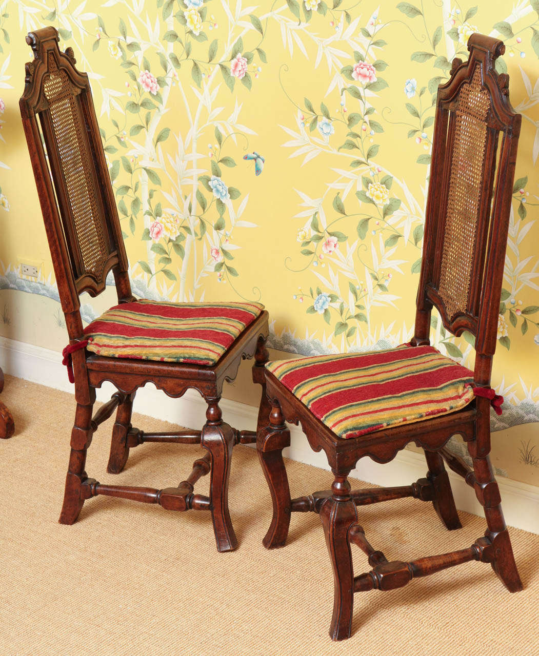 Rare pair of William & Mary period carved walnut tall back side chairs, each with a scrolled shaped moulded top rail, above matching stiles centering a caned splat with slim cushions on the caned seats and a shaped incised apron above hipped incised