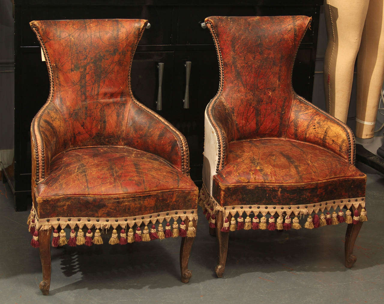 Unusual pair of curvy faux finished leather child size chairs trimmed in tassels and nailheads, as found.