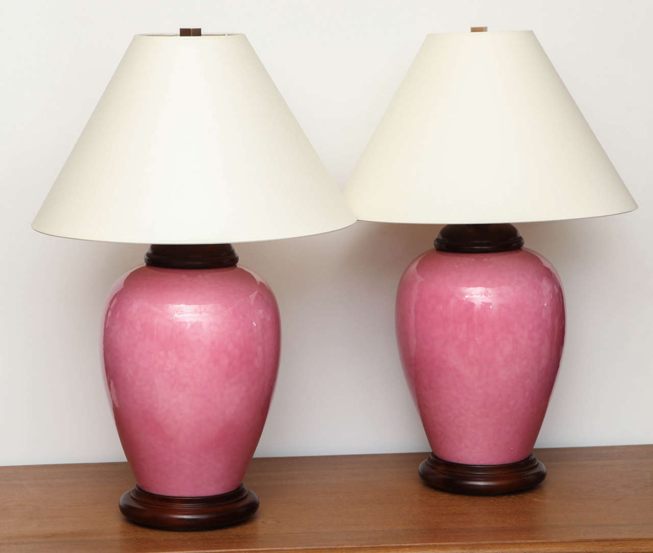 Pair of rose colored ceramic urn shaped lamps with wood base and cap. Shades not included.
