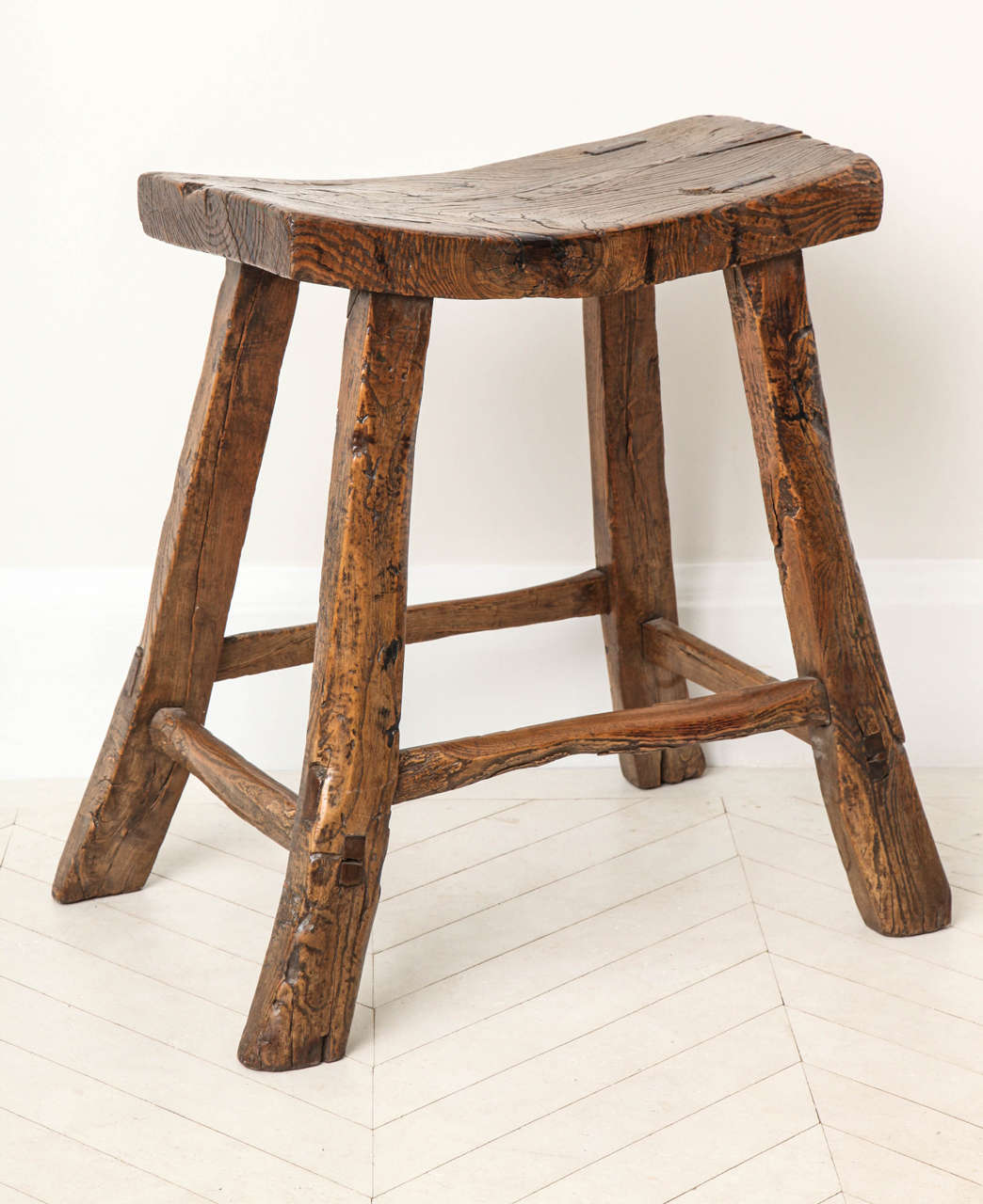 A 19th century Chinese elm wood stool with sloped seat, splayed legs, pegged construction and an overall mellow patination