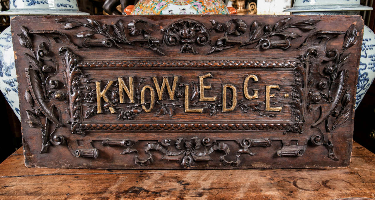 Carved of probably walnut, this sign has gilded lettering, within a gadrooned border with leaves, flowers and vines. Probably from a library or school.