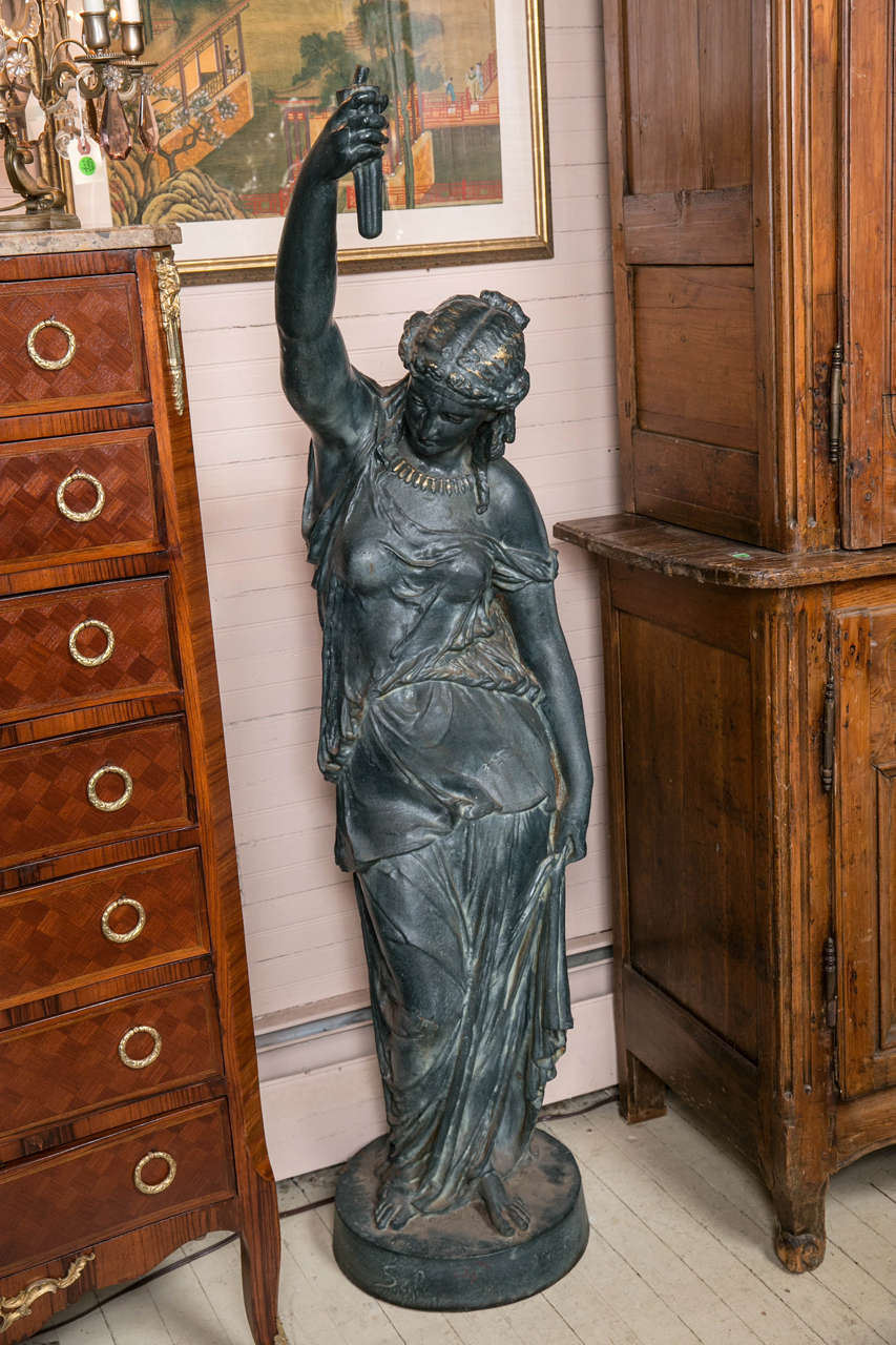 A draped female figure holding her   right arm a lot. In her hand she holds  the base of possibly a torch. Signed on the base Salin, Paris. The  Salin Foundry. 
   round base . the arm projects approximately  18 inches.
