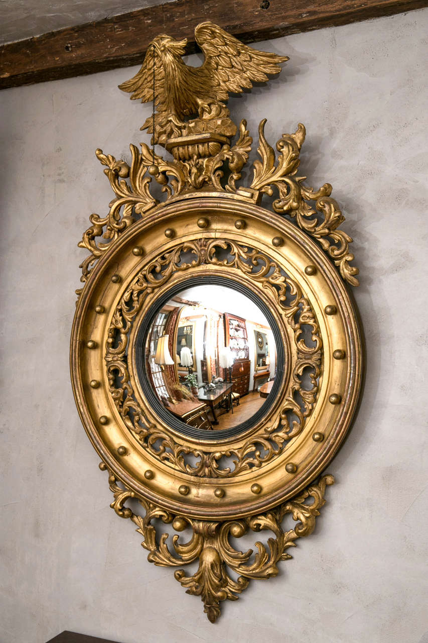 This convex mirror with carved, gilded frame and eagle surmounted pediment deviates from the norm by featuring an open fret frame that, while adding interest, subtracts some of the visual weight that comes with such a large and complex frame.