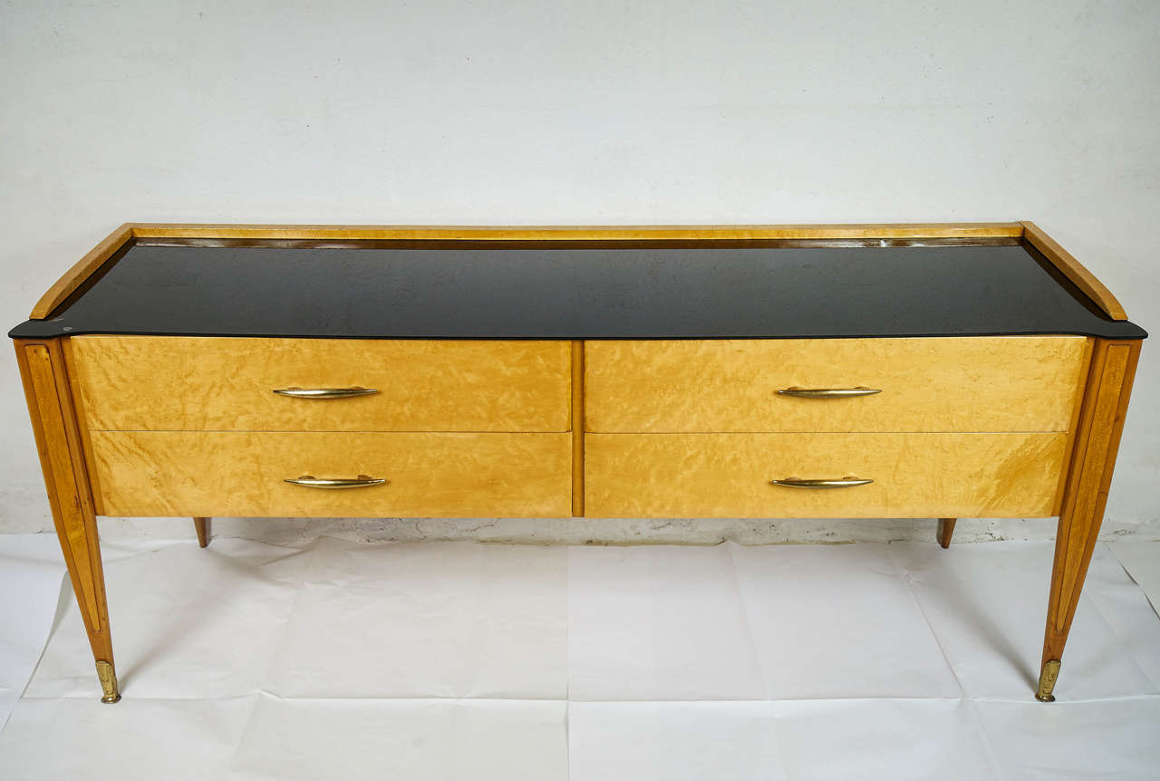  Four drawers solid maple wood and bird eyes maple chest  brass feet and handle details.
Top on black glass.
Four slender leggs ending with brass feet.