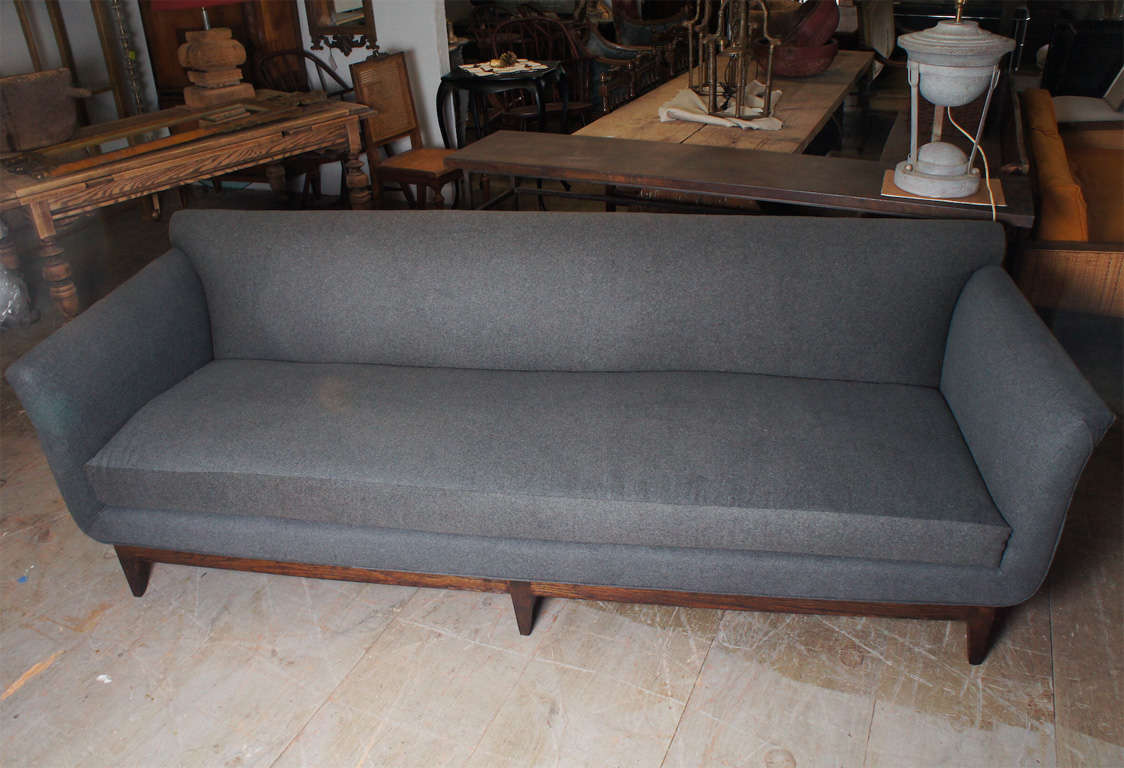 Mid century modern tailored grey flannel wool newly upholstered sofa with flared arms and dark walnut stained base.