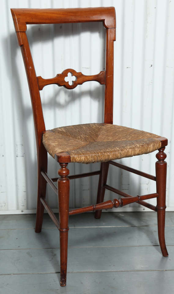 A set of four Gothic-style dining chairs with rush seats. Chairs have a cherry finish. Rush seats are original. Seat height: 17