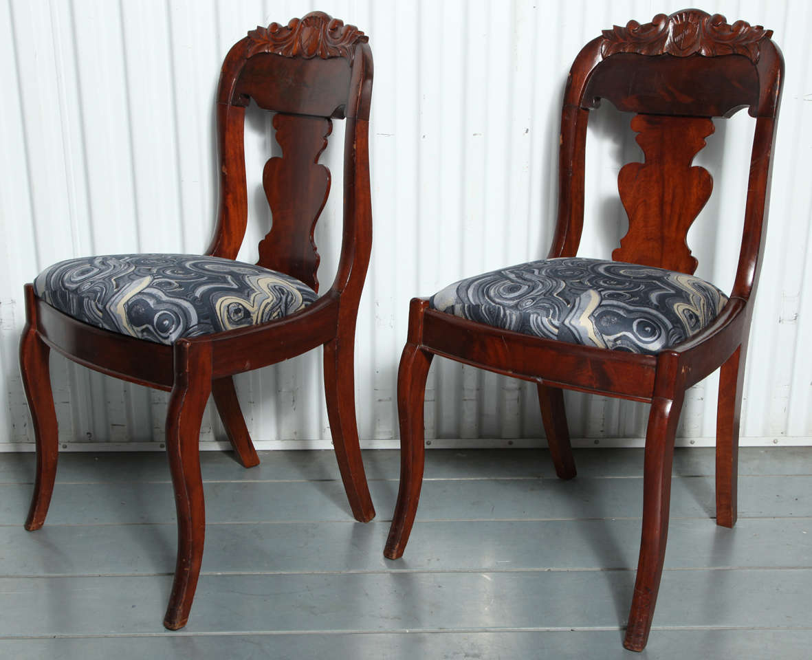 A pair of newly upholstered 19th Century wood-framed hall chairs with scrolled backs and carved leaf and shield detail. Upholstery fabric is a malachite cotton pattern from the Tony Duquette collection for Jim Thompson.