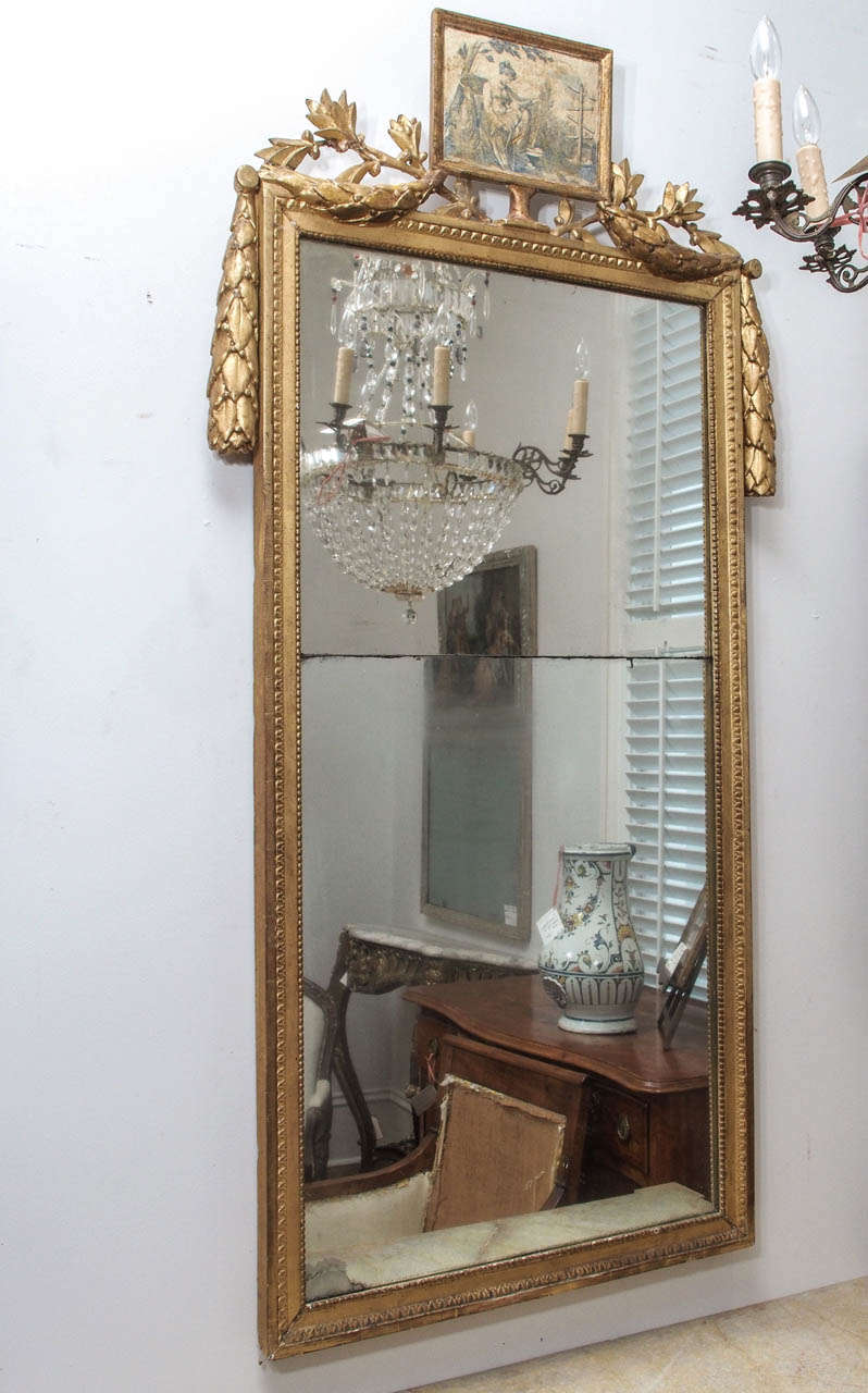 A large, 19c. giltwood mirror with crossed olive branches supporting a small framed grisaille painting,  the sides flanked with hefty garlands of leaves and berries.  The glass in two parts.  This mirror would have originally had an urn or other