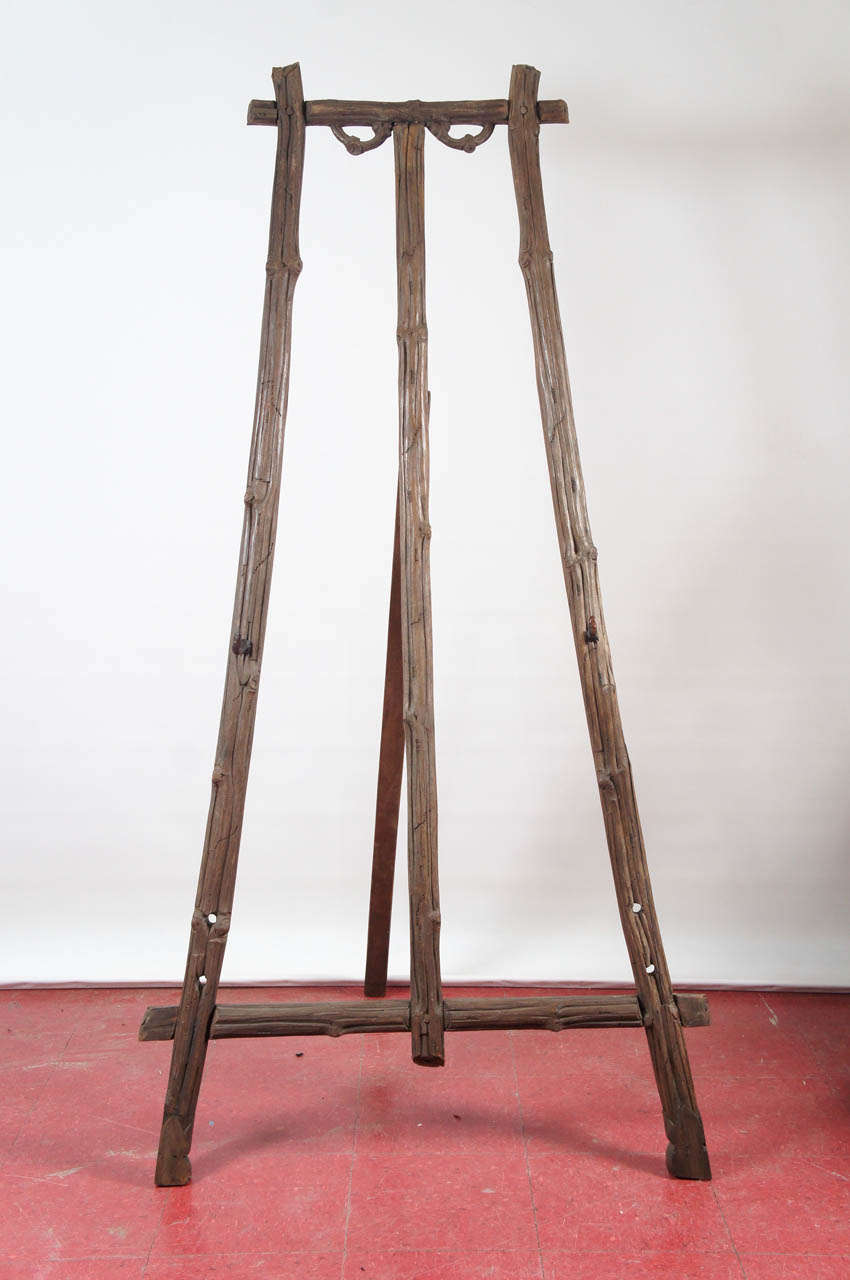Well made and sturdy, this antique German easel is carved in wood, representing rustic tree branches.  The brace can be flattened against the easel for storage purposes.  A pair of L-shaped brackets can be moved to three different positions