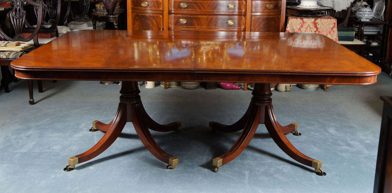 This Sheraton style table has a fine mellow color, with reeded border and small apron. The bases are cannon shaft columns with reeded sabre legs ending in four splayed feet capped in brass with brass casters. 
This fabulous dining room table