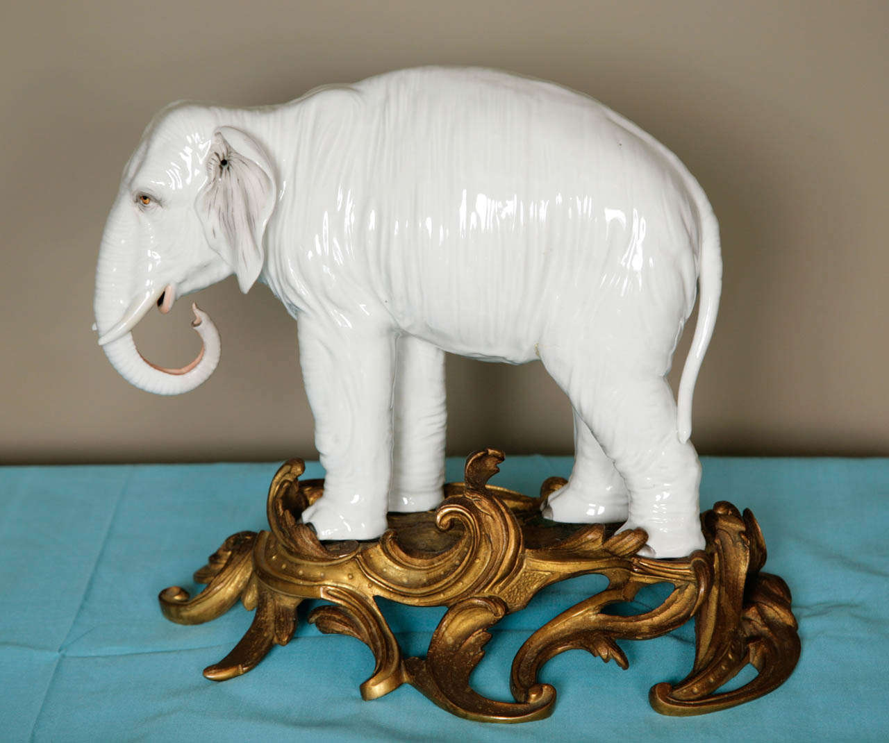 A finely modelled white porcelain elephant standing with left foot forward, trunk curled beneath tusks, the features realistically picked out in colours mounted on a gilt bronze ormolu base. Possibly Elbogen Porcelain Factory.
Comparative example