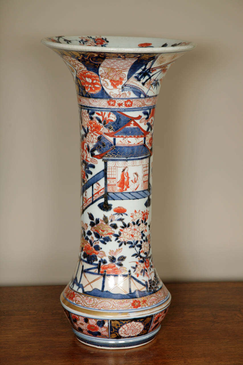 This is a very large Imari sleeve vase and stands at 23inches/59 cm high. Decorated with panels, flowers and Japanese ladies in tea pavillions. In primary Imari colours of blue, red and gold. A real Country House piece.