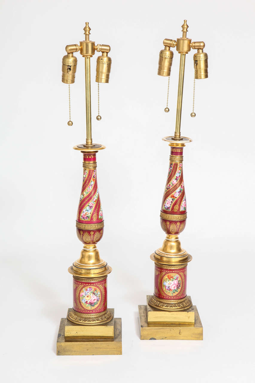 Pair of antique French Empire red porcelain and ormolu-mounted lamps, attributed to Sèvres. The porcelain bases of the lamps are decorated with ovals depicting bouquets of hand painted multicolored flowers on a red porcelain background. The main
