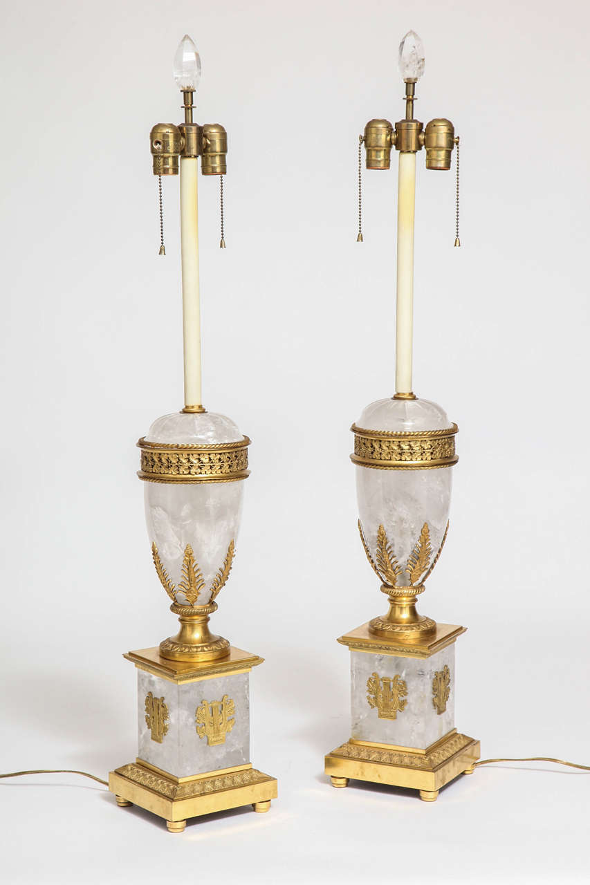 Extraordinary pair of antique French neoclassical and Empire style rock crystal and ormolu lamps. Rock crystal at the base is adorned with decorations of the classical instrument the Lyre. An ormolu band of laurel leaves ring the rock crystal column