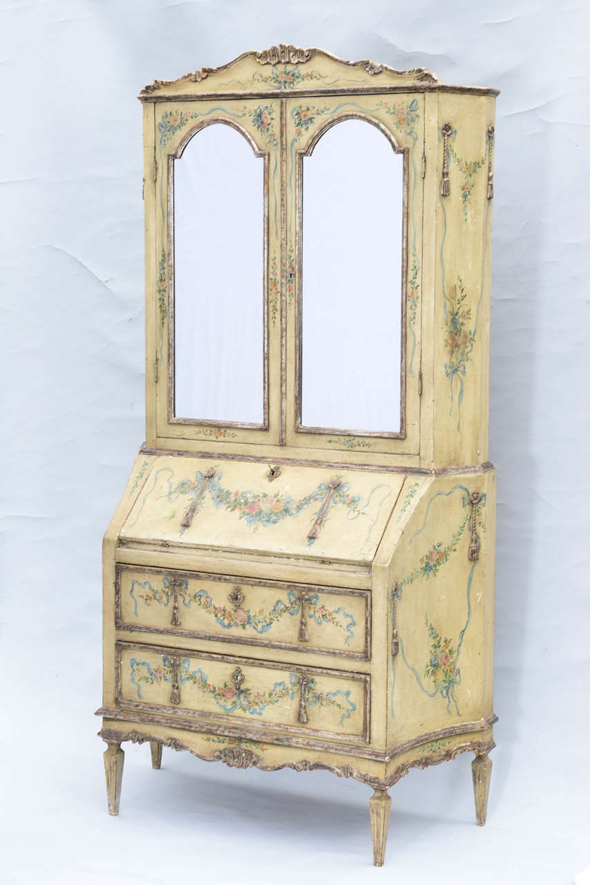 Outstanding example of a Venetian bureau bookcase, or secretaire, having a serpentine cornice surmounted by foliate carving, over double cupboard doors inset with arched mirrors, fall-front desk revealing cubbies and drawers, over double stack