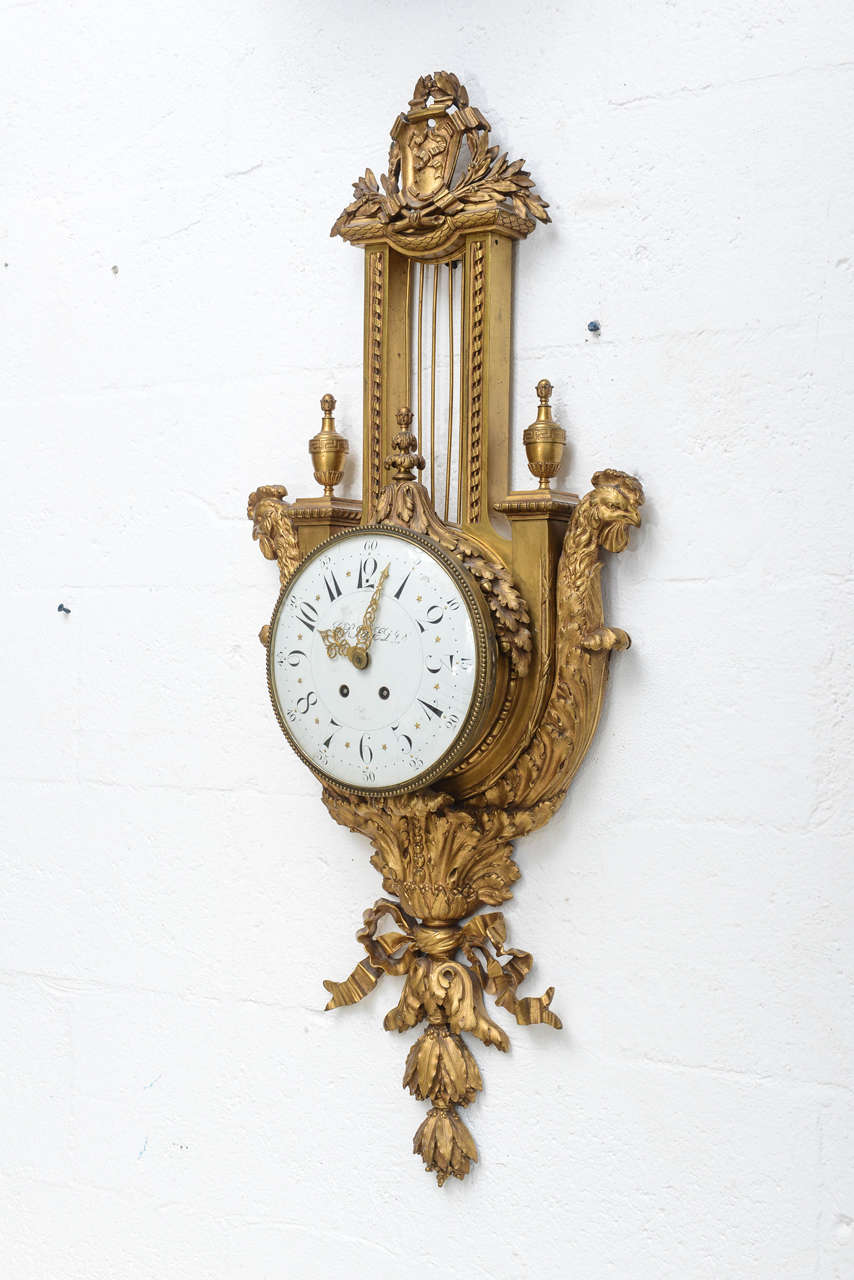 Fine wall clock, of dore bronze, in the Louis XV style, having round enamel clock face surmounted by acanthus leaf, gadrooning and urn details, flanked by finely chased "tetes de coqs" finials, and terminating in elaborate acanthus and