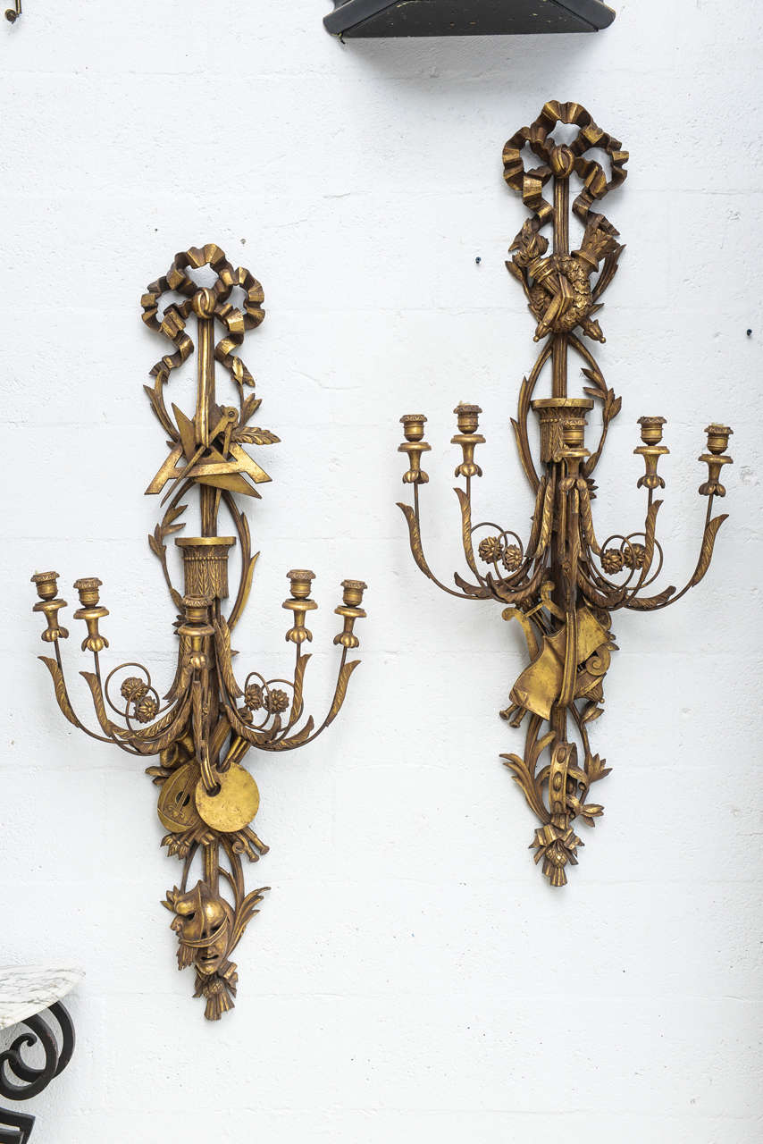Opposing pair of large scale giltwood wall lights, each elaborately carved representing the arts and sciences, surmounted by a bow, having three C-scroll candlearms  ending in wooden candlepots. Not electrified.