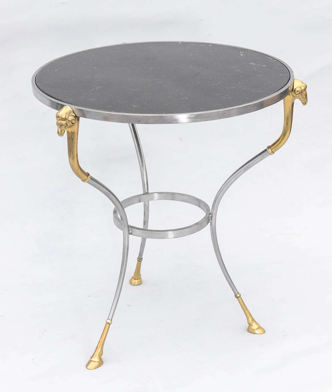 Gueridon, having black veined marble top inset in steel frame, raised on three legs each surmounted by a brass ram's head and terminating in a hoof foot, connected by a round stretcher.

Stock ID: D9175
